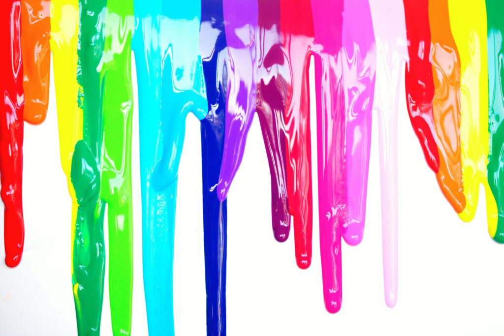 Bright, colorful paints dripping creating a rainbow effect on a white background, symbolizing diversity and creativity.